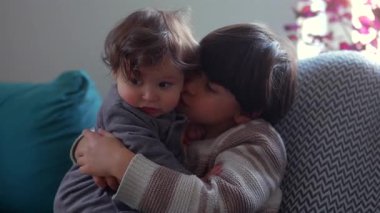 Ağabey, küçük çocuğu yanağından öpüyor. Kardeşine yakın, samimi bir kardeş gibi sımsıkı sarılıyor. Sıcak, şefkatli ve aile şefkati dolu bir evde.