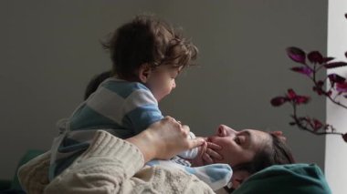 Bebek annesinin yüzüne dokunmak için öne eğiliyor, anne uzanırken gülümsüyor, neşeli ebeveyn çocuk şefkati, güveni ve gerçek duygusal bağlantıyı çağrıştırıyor.