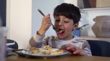 Çocuk mutfak masasında kahvaltı yaparken çatalla waffle kaldırıyor.