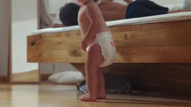 Bebek bezi giymiş, ayağa kalkmış ve yatak odasından kameraya doğru yürüyordu. Kardeşinin sıcak ev ortamında yatakta dinlendiği neşeli bir sabah anıydı.