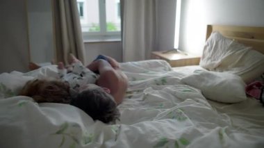 Küçük çocuk neşeyle gülerken ağabeyi neşeli bir sabah yatağında ona sarılıyor, kardeş sevgisi kavramı, kaygısız aile bağı ve mutlu çocukluk anları.