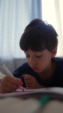 Çocuk yatakta yatarken keçeli kalemle resim çiziyor, yaratıcı aktivite sırasında odaklanmış ifade ve evde öğreniyor..