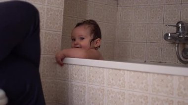 Bebek küvette gülümsüyor, anne babaya bakıyor, banyo zamanı, oyun ve sevgi dolu sıcak ev ortamında.