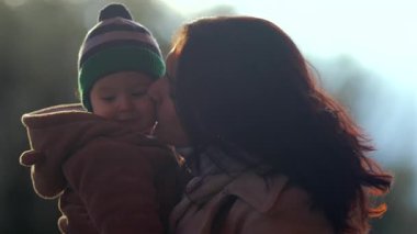 Anne bebeği yanaktan öperken çocuk ayıcık postu giyer ve açık havada çizgili şapka takar. Ebeveyn, aile bağları sırasında sevgi ve sevgi gösterir..