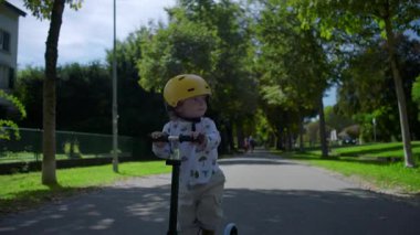 Küçük çocuk park yolunda sarı kasklı scooter sürüyor, çocukluk oyunu ve macera, açık hava yaşam tarzı, güvenlik ve neşe ile kaygısız boş zaman anı