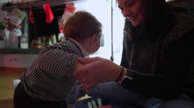 Anne gülümserken yeni yürümeye başlayan çocuğa oturma odasında ayakta durmasını öğretiyor, ebeveynlik desteği, çocukluk gelişimi, aile bağı ve erken öğrenme kilometre taşı konsepti.