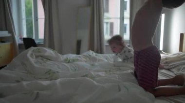 Kardeşler yatak odasında neşe içinde zıplayıp düşüyorlar. Kardeş bağı, neşeli çocukluk enerjisi, aile birlikteliği ve kaygısız ev hayatı kavramı.