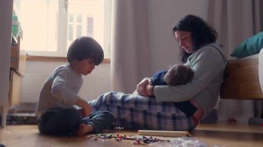 Anne yatak odasında bebeği emzirirken büyük çocuk aile bağları sırasında renkli oyuncaklarla oynuyor.