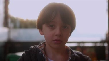 Dışarıdaki çocuk düşünceli bir ifadeyle yan tarafa bakıyor. Öğleden sonra ışığında sakin bir aile ortamında sıradan bir ceketle oturan çocuk..