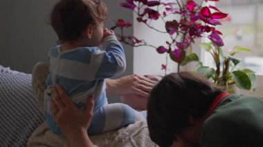 Anne kanepeye uzanıyor, bebek göğsünde ve büyük çocuk yanında, hassas aile bağları ve evde birliktelik.