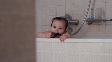 Bebek banyo sırasında küvette oturup çiğneme oyuncağı, çocukluk çocukluk merakı, keşif ve masumiyet anı sıcak ev ortamında.