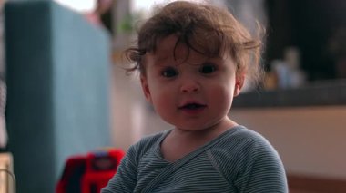 Bebek yerde otururken gülümsüyor, masumiyetin, oyunun ve keşiflerin meraklı bebek ifadesi günlük aile ortamında.