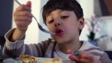 Çocuk kahvaltısını yaparken çatal ve waffle 'ı ağzına doğru ısırıyor..