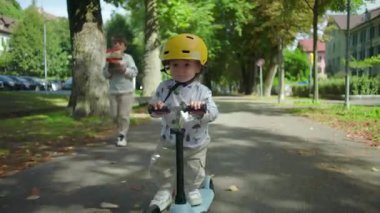 Yakın plan yürümeye başlayan çocuk parkta skuter sürerken sarı miğfer, neşeli bir an, büyük kardeş oyuncak uçak tutarken, kaygısız çocukluk sahnesi