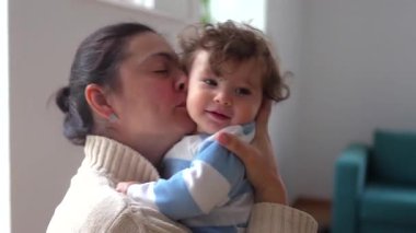 Anne kucağında mutlu bir bebekle gülümsüyor. Oturma odasında sevgi ve sıcaklık gösteriyor..