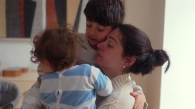 Anne evde iki küçük çocuğa sarılıyor sevgi ve duygusal yakınlık gösteriyor sevgi dolu bir aile ortamında..