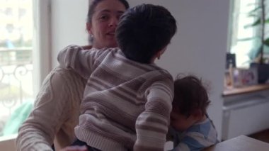 Bebek evde yemek yerken kucağında oturan büyük çocuk annesine sarılıyor.