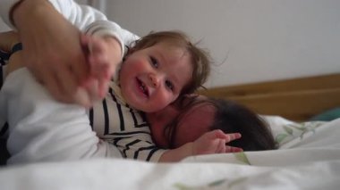 Bebek neşeyle gülerken anne yatakta gıdıklanıyor ve sarılıyor. Sevgi, kahkaha ve enerjik aile mutluluğuyla dolu neşeli bir bağ anı..