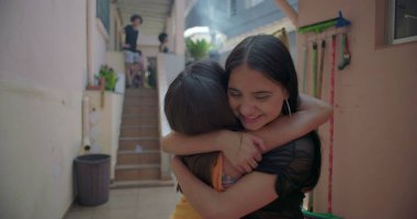 Latin kökenli iki genç kız banliyöde sarılıp gülüyorlar, neşeli ve eğlenceli bir an, arkadaşlığı ve çok kültürlü kimliği temsil ediyorlar.