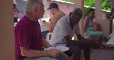 Avluda yemek tabakları, rahat toplanma, sosyal etkileşim, nesiller arası topluluk, tropikal ortam tutarken yaşlı erkekler sohbet ediyorlar.