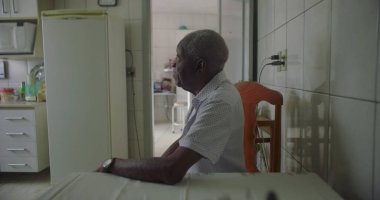 Bir yaşlı siyah adam mutfak masasında oturmuş, kollarını dinlendiriyordu. Etrafı fayanslarla, duvarlarla, buzdolabıyla ve rahat bir ev ortamında ahşap sandalyelerle çevriliydi.