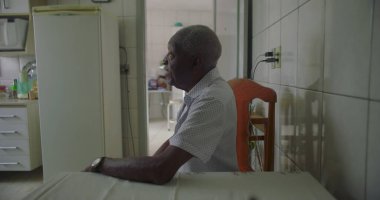 Bir yaşlı siyah adam mutfak masasında oturmuş, kollarını dinlendiriyordu. Etrafı fayanslarla, duvarlarla, buzdolabıyla ve rahat bir ev ortamında ahşap sandalyelerle çevriliydi.