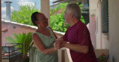 Yaşlı çift açık hava aile toplantısı sırasında dans ediyor ve gülüyor. Keyifli ve keyifli bir atmosferde neşeli bir anın tadını çıkarıyorlar.