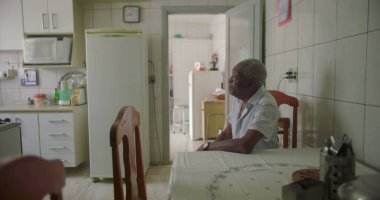 Bir yaşlı siyah adam mutfak masasında oturmuş, kollarını dinlendiriyordu. Etrafı fayanslarla, duvarlarla, buzdolabıyla ve rahat bir ev ortamında ahşap sandalyelerle çevriliydi.