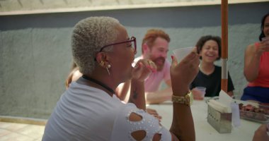 Sarışın, kısa saçlı, gülen ve bardağını kaldıran bir kadın arka bahçede barbekü yaparken arkadaşlarıyla birlikte yazın neşe ve bağlarını paylaşıyor.