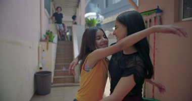 Latin kökenli iki genç kız banliyöde sarılıp gülüyorlar, neşeli ve eğlenceli bir an, arkadaşlığı ve çok kültürlü kimliği temsil ediyorlar.
