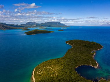 Adriyatik Denizi 'nin dağınık yeşil adaları ve Hırvatistan' da bir dağ zeminiyle çarpıcı bir görüntüsü. Derin mavi su ve canlı yeşillik bunu büyüleyici bir manzara yapar.