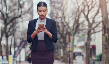 Yoldayım, bir kaç dakika içinde seninle buluşacağım. Şehirde dolaşırken akıllı telefon kullanan çekici genç bir iş kadını.