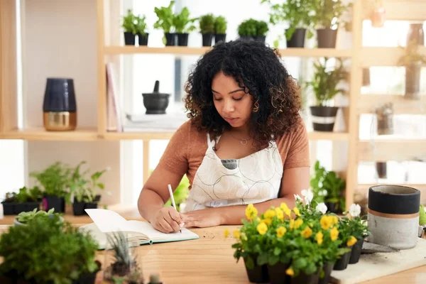 Making a note of her orders for the day. an attractive young female botanist making notes while working in her florist