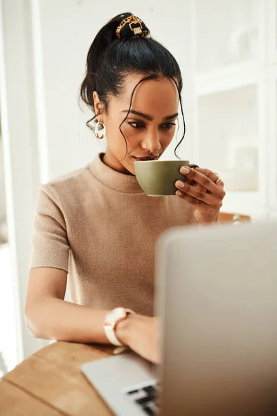 Stock image Coffee and technology go hand in hand. an attractive young businesswoman sitting and enjoying a cup of coffee while using her laptop at home