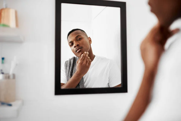 I think I prefer the no beard look. a young man touching his face while looking into the bathroom mirror