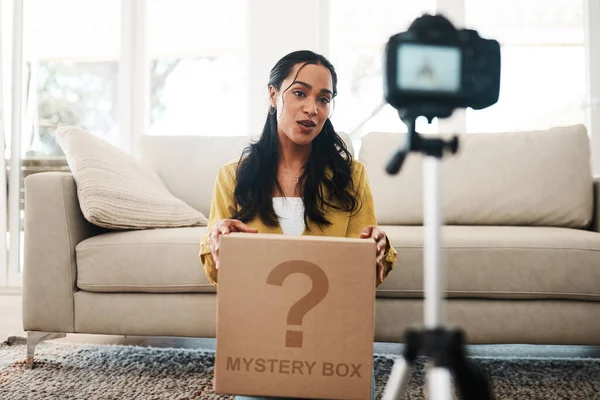 Updating my followers on my current life. an attractive young businesswoman sitting in her living room and holding up a mystery box while vlogging