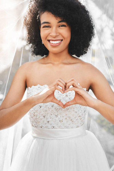 Were celebrating true love today. Portrait of a happy and beautiful young bride making a heart shape with her hands outdoors on her wedding day