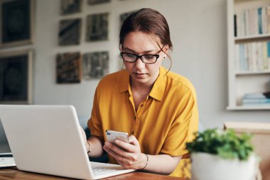 Yan koşuşturması şekillenmeye başlıyor. Evden çalışırken akıllı telefon ve laptop kullanan genç bir kadın.