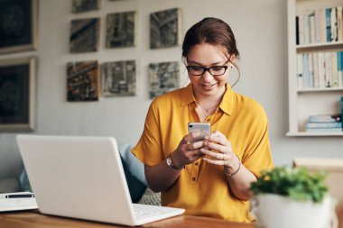 Küçük bir işletme sahibi için en iyi ağ aracı. Evden çalışırken akıllı telefon ve laptop kullanan genç bir kadın.