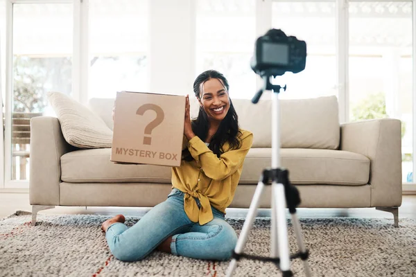 Showing my fans the special surprise I have in store. Full length shot of an attractive young businesswoman sitting in her living room and holding a mystery box while vlogging