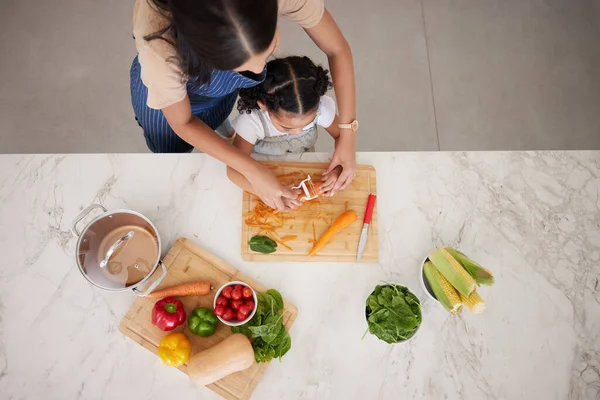 Cooking, vegetables and mom with child in kitchen cutting, peeling and prepare food. Child development, helping hands and aerial view of mother teaching girl to cook, chef skills and bond together.