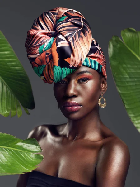A head wrap enriched with history. Studio shot of a beautiful young woman wearing a traditional African head wrap against a leafy background