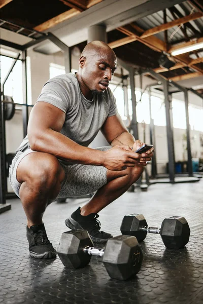 Fitness, phone and online personal trainer at the gym typing or searching on social media in Nigeria. Strong black man, bodybuilder and healthy sportsman networking or texting a digital message.