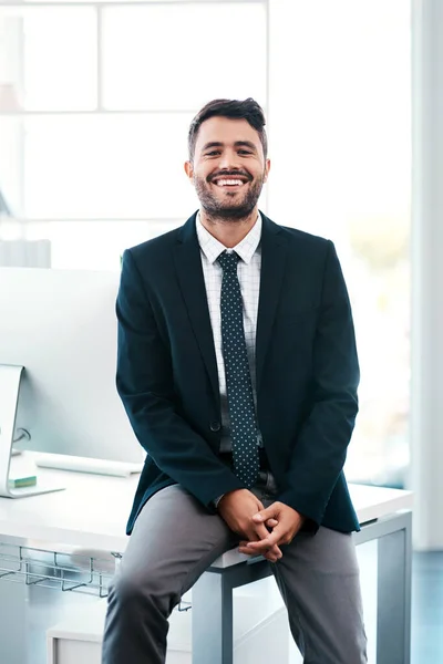 Hard work got me here. Cropped portrait of a handsome young businessman smiling while sitting on his desk in a modern office