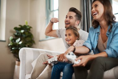 Ailenle zaman geçirdiğinde zaten kazanırsın. Mutlu, genç bir aile evdeki kanepede oyun oynuyor.