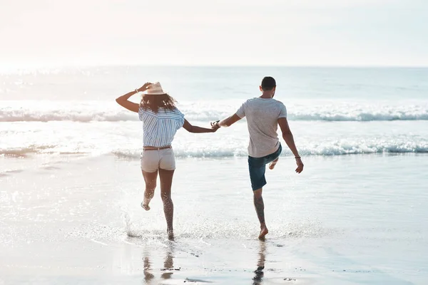 感受夏天的精神一对年轻夫妇在海滩上在水里飞溅的后视镜镜头 — 图库照片
