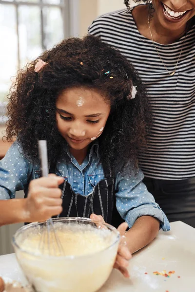 Its getting messy in the kitchen. a little girl baking at home with her mothers help