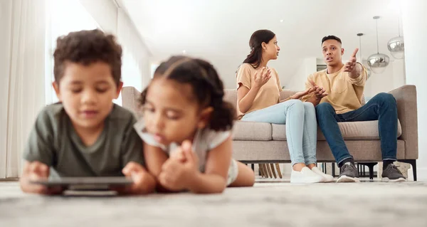 Mother, father and disagreement on living room sofa while children are playing with tablet on the floor at home. Mama and dad fighting, argue or conflict in difficult situation on couch in dispute.