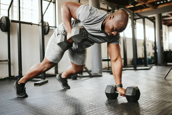 Dumbbell, fitness and bodybuilder black man with workout training in gym or garage studio for wellness, body goal and motivation. Power, strong and african sports man doing push up exercise with gear.
