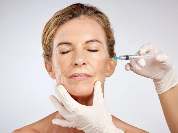 Botox, surgery and face with mature woman getting an injection in her cheek for beauty, skincare and medicine in studio on a blue background. Filler, product and cosmetics with a female model inside.